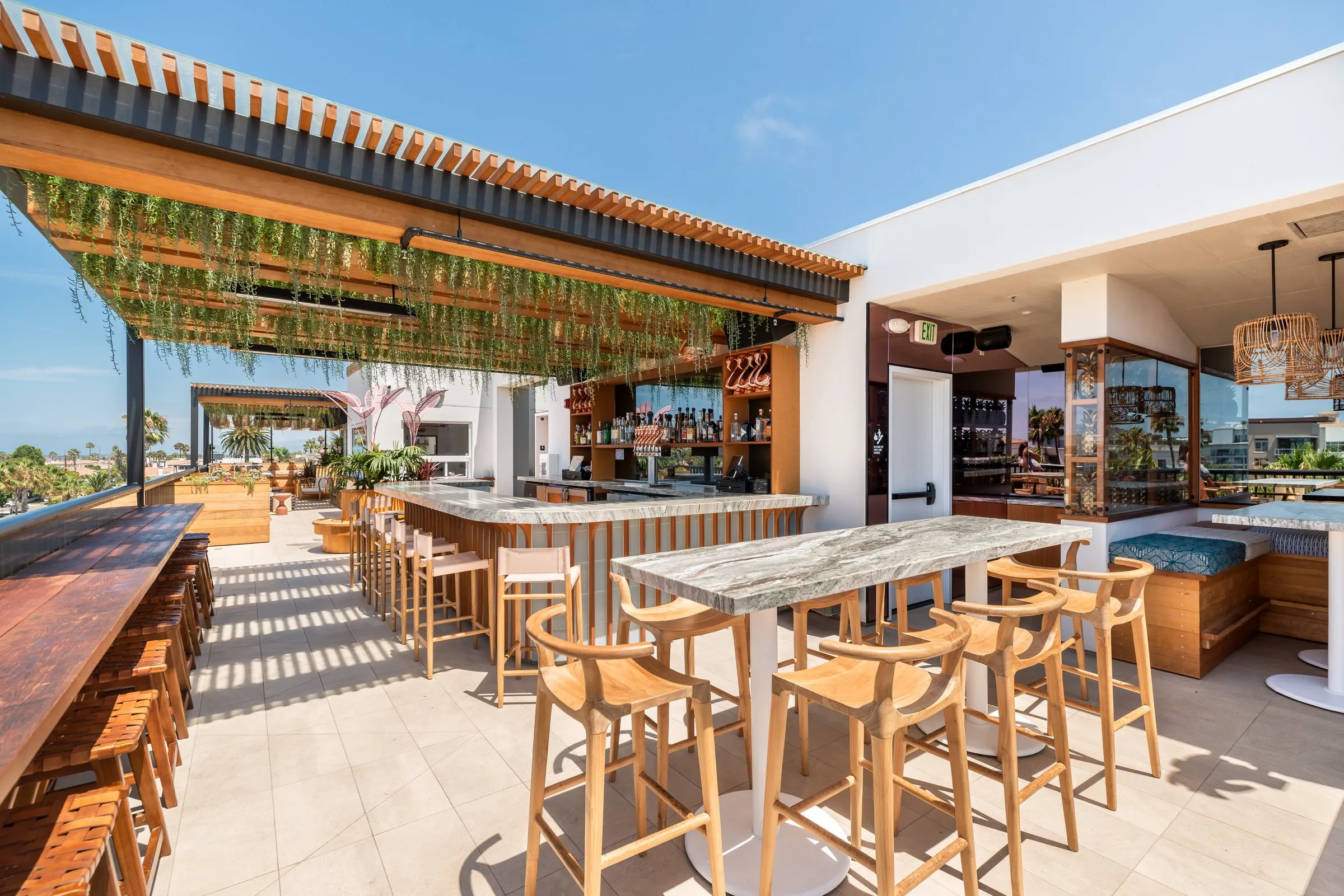Coco Cabana open-air rooftop bar — marble counter, bar stools, hanging greenery, Oceanside views
