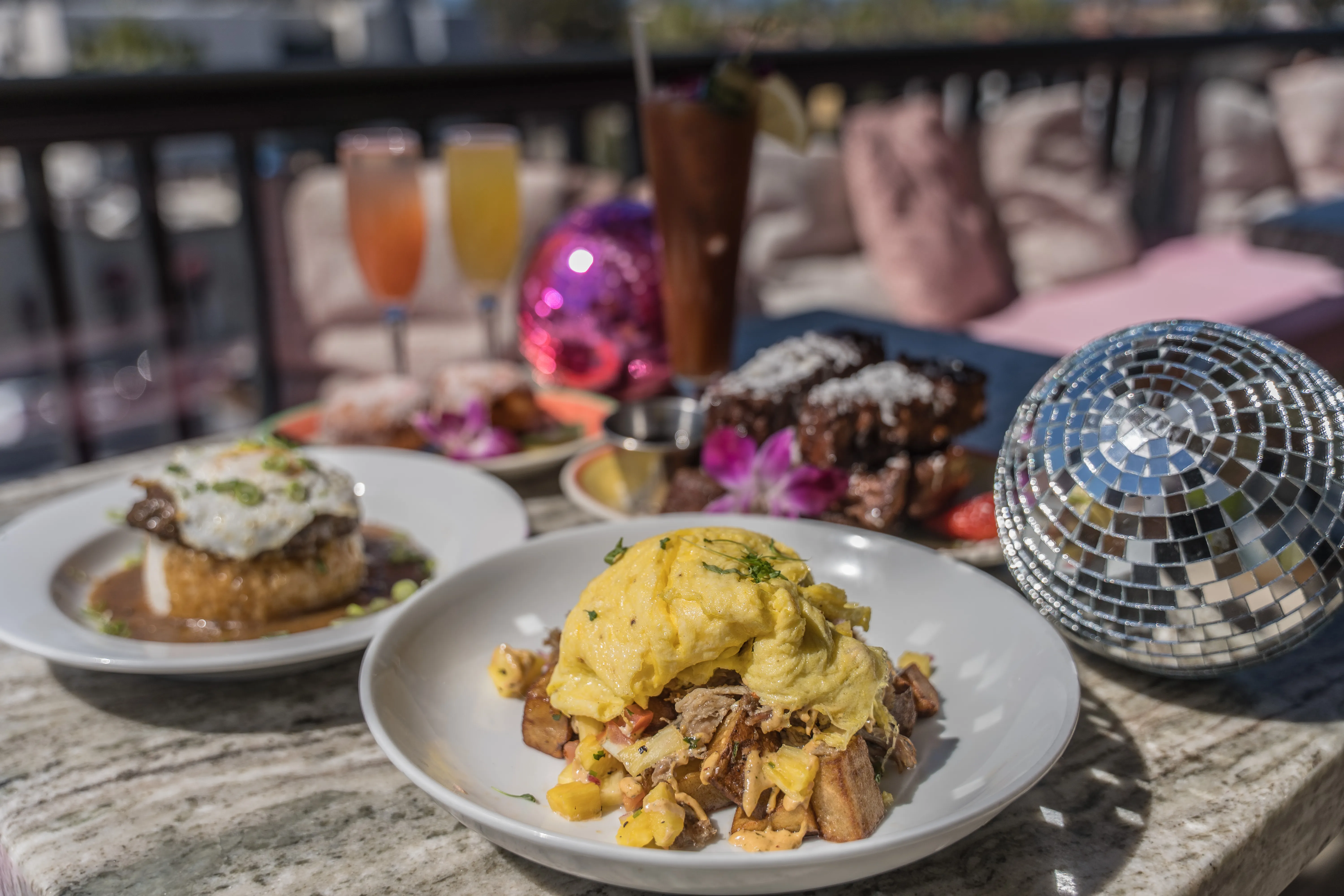 Scrambled eggs over roasted hash with disco balls and palms in background
